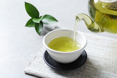 Photo of Pouring green tea into white porcelain cup on light table