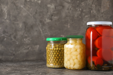 Photo of Glass jars with different pickled vegetables on grey table. Space for text