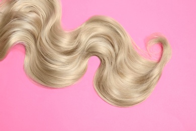 Lock of blonde wavy hair on color background, top view