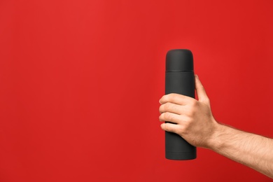 Photo of Man holding black thermos on red background, closeup. Space for text
