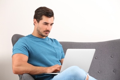 Handsome young man working with laptop on sofa indoors