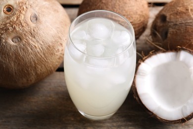 Glass of coconut water, ice cubes and nuts on wooden table