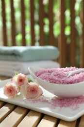 Photo of Bowl of pink sea salt and beautiful roses on wooden table, closeup. Space for text
