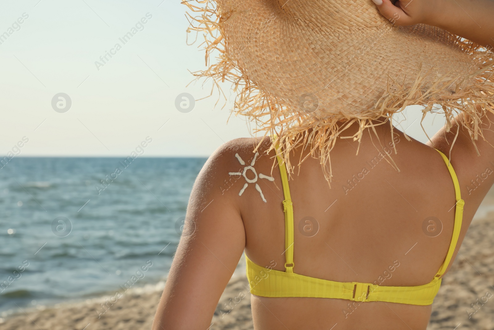 Photo of Young woman with sun protection cream on shoulder at beach, back view