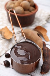 Photo of Measuring cup with tasty tamarind sauce and fresh pods on white wooden table
