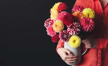 Photo of Woman with bouquet of beautiful dahlia flowers on black background, closeup. Space for text