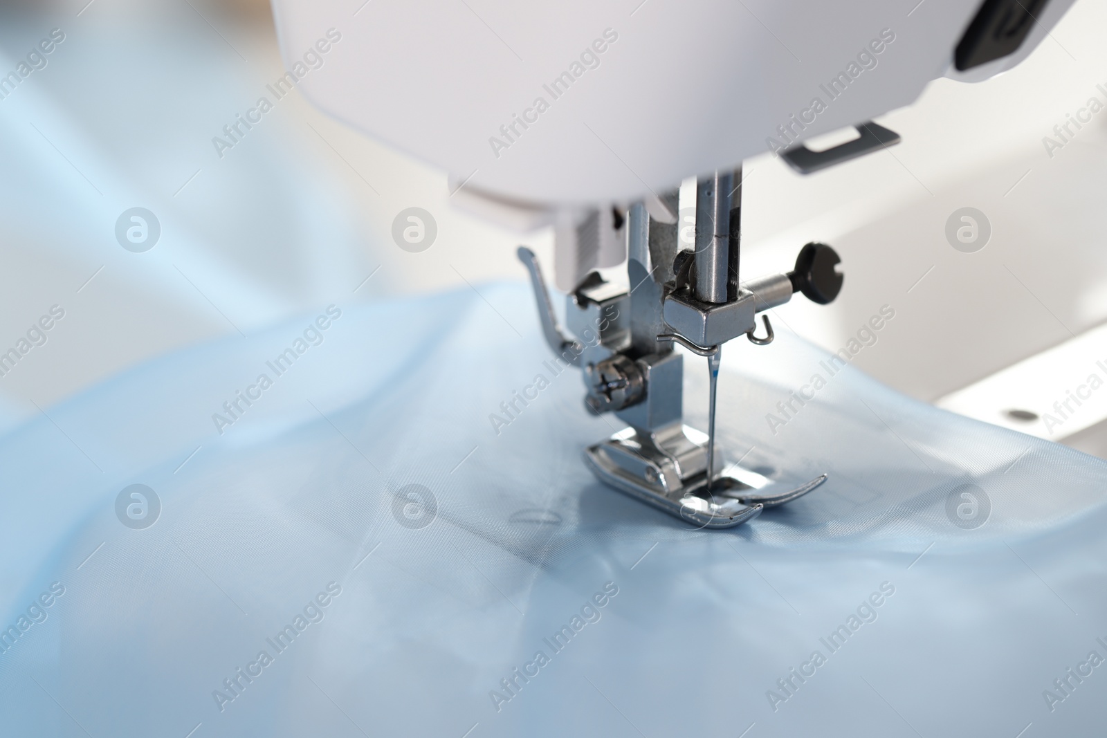 Photo of Sewing machine with light blue fabric, closeup