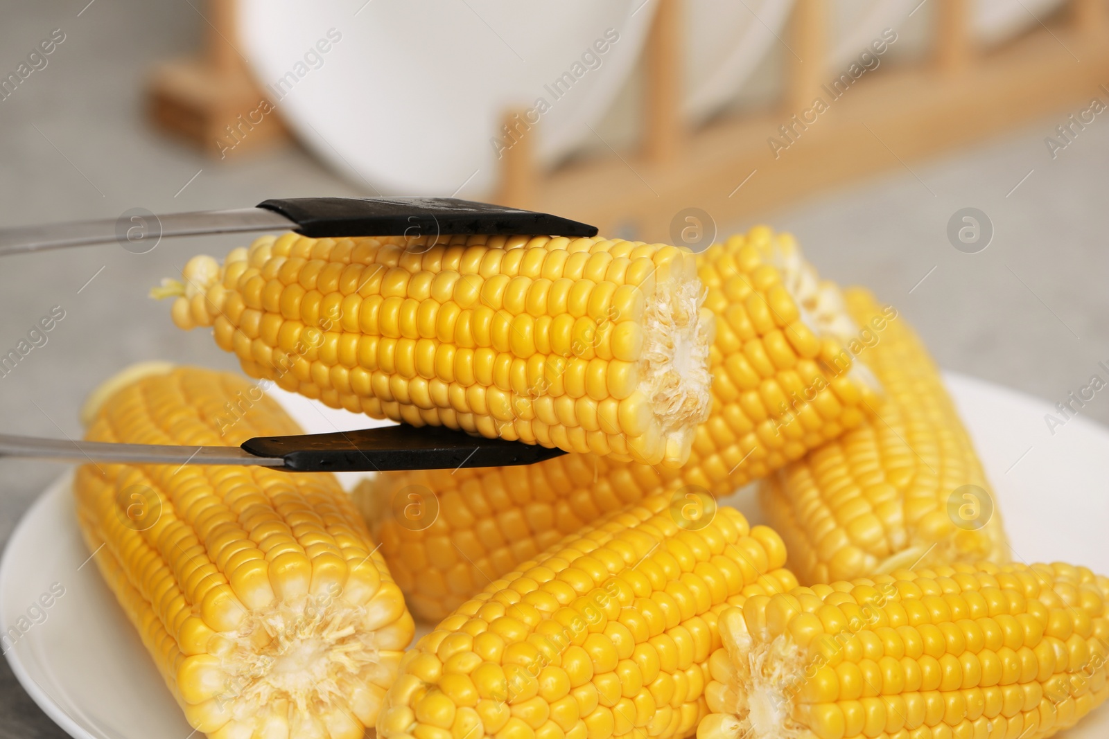 Photo of Taking corn cob from plate with tongs, closeup