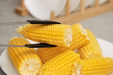 Taking corn cob from plate with tongs, closeup