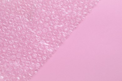 Photo of Transparent bubble wrap on pink background, top view. Space for text