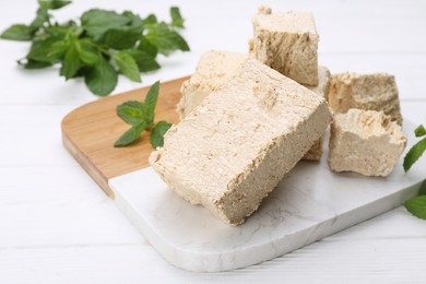 Photo of Pieces of tasty halva and mint on white wooden table, closeup. Space for text