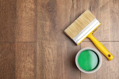 Can of green paint and brush on wooden background, flat lay. Space for text