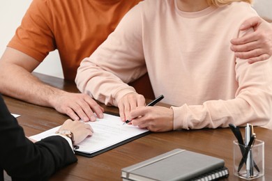 Photo of Notary helping couple with paperwork at wooden table, closeup