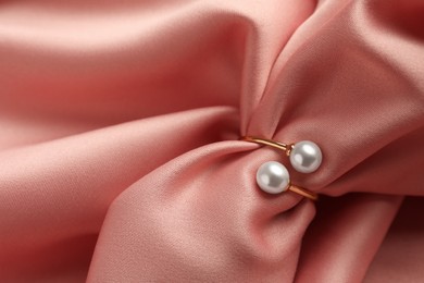 Photo of Elegant golden ring with pearls on pink silk, closeup