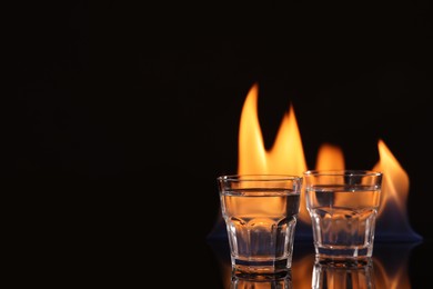 Photo of Vodka in glasses and flame on black background, space for text