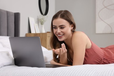 Photo of Happy woman having video chat via laptop on bed in bedroom