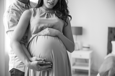 Pregnant woman with her husband indoors, black and white effect. Space for text