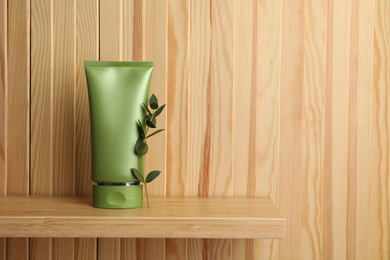 Photo of Tube of cosmetic product and plant on shelf near wooden wall, space for text