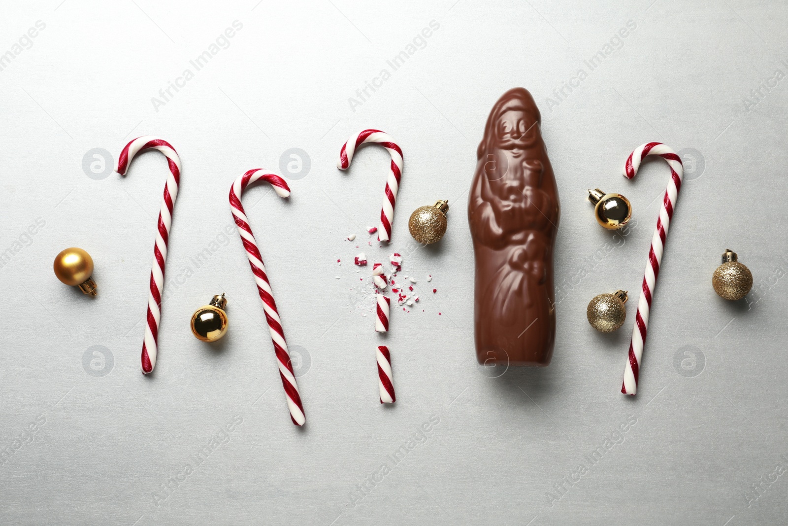 Photo of Flat lay composition with chocolate Santa Claus, candy canes and Christmas balls on light grey background