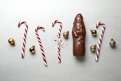 Photo of Flat lay composition with chocolate Santa Claus, candy canes and Christmas balls on light grey background