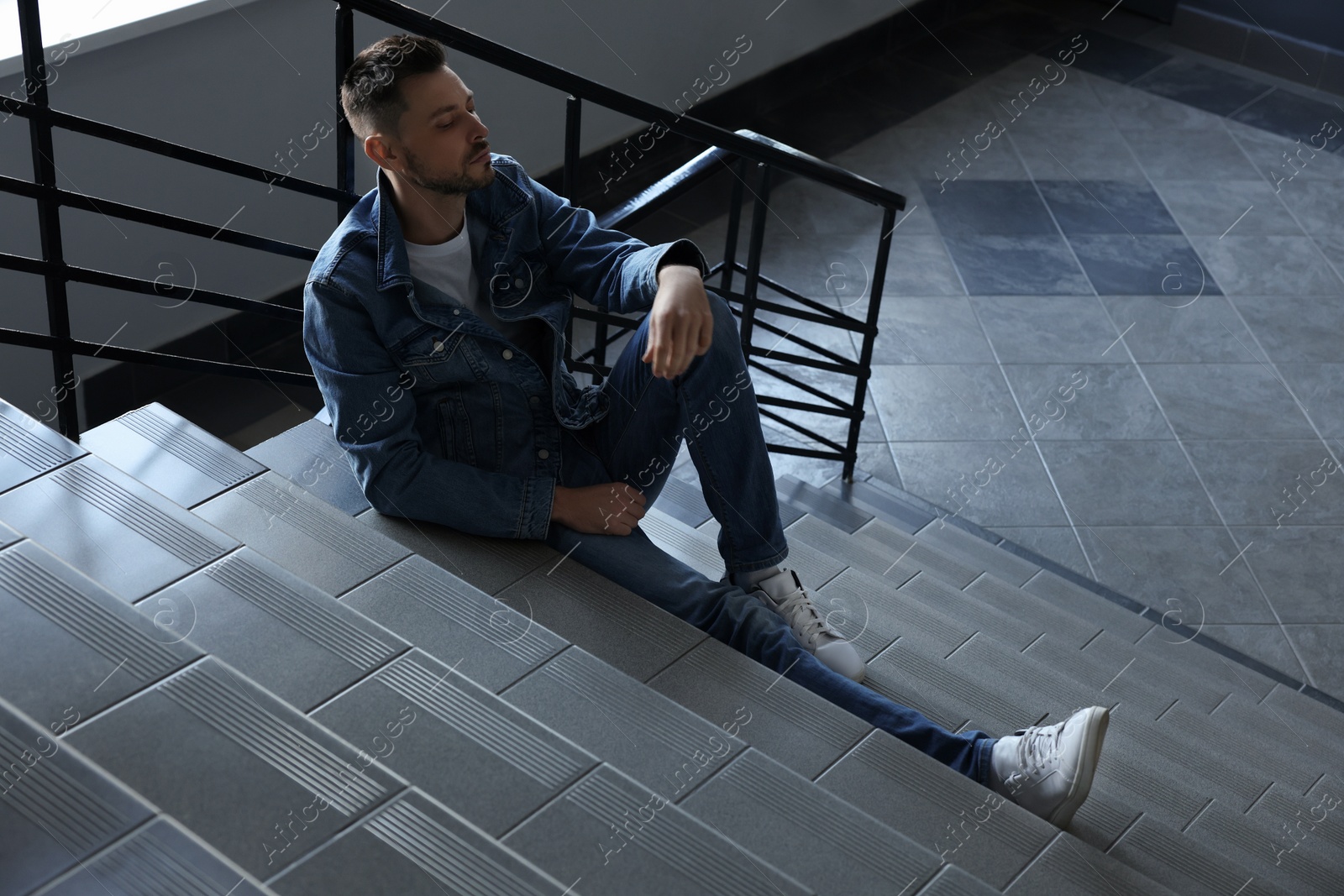 Photo of Upset man sitting on stairs indoors. Loneliness concept