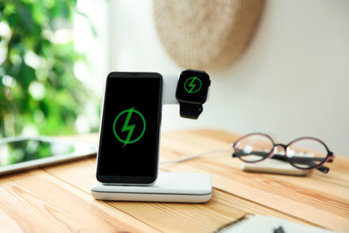 Photo of Mobile phone and smartwatch with wireless charger on wooden table. Modern workplace accessory