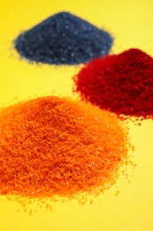 Photo of Heaps of different bright food coloring on yellow background, closeup