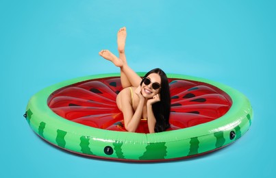 Young woman in stylish sunglasses on inflatable mattress against light blue background