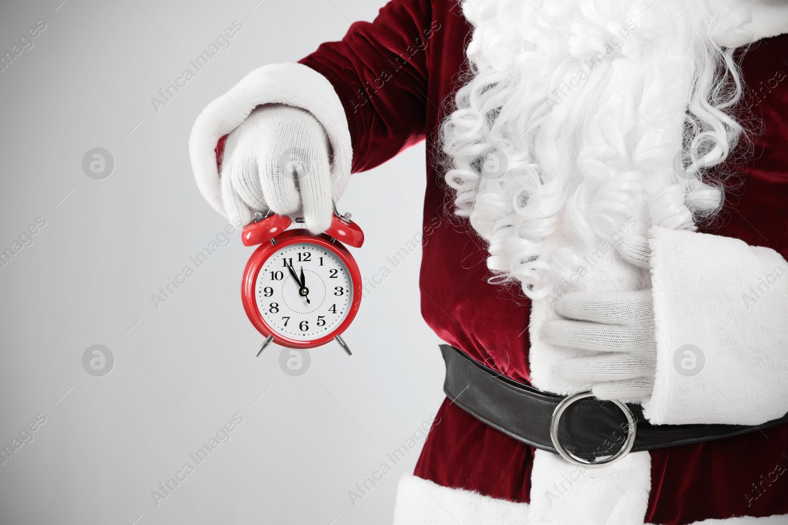 Photo of Santa Claus holding alarm clock on light grey background, closeup. Christmas countdown