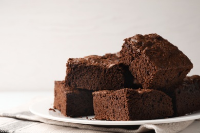 Plate with fresh brownies on white table against light background, space for text. Delicious chocolate pie