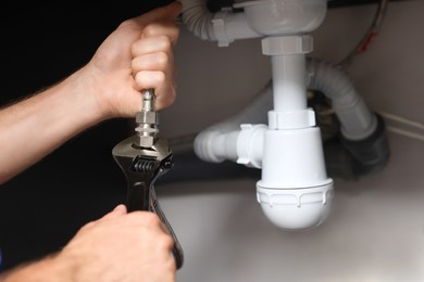 Photo of Professional plumber with adjustable wrench fixing sink indoors, closeup