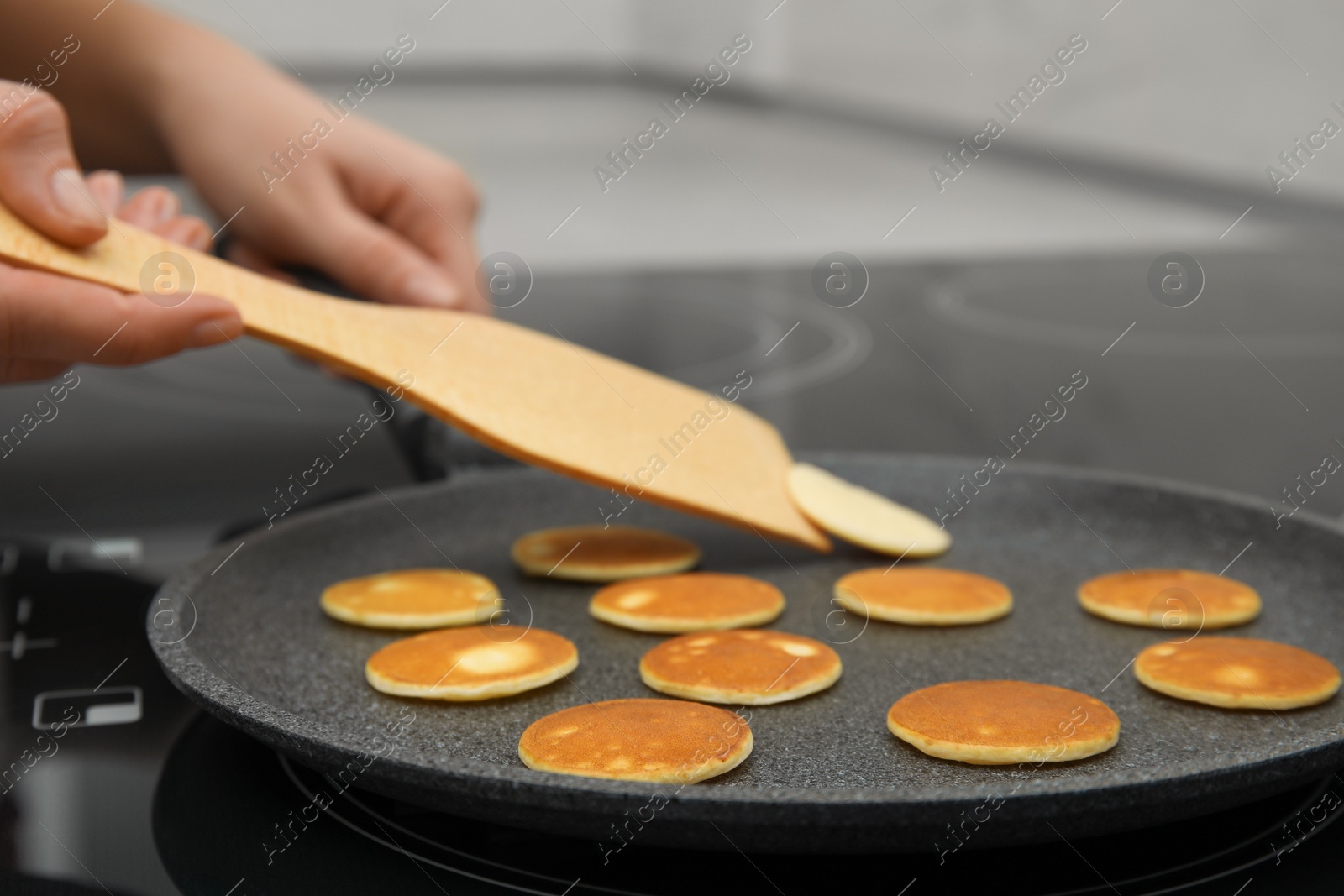 Photo of Woman turning cereal pancake with spatula on stove, closeup