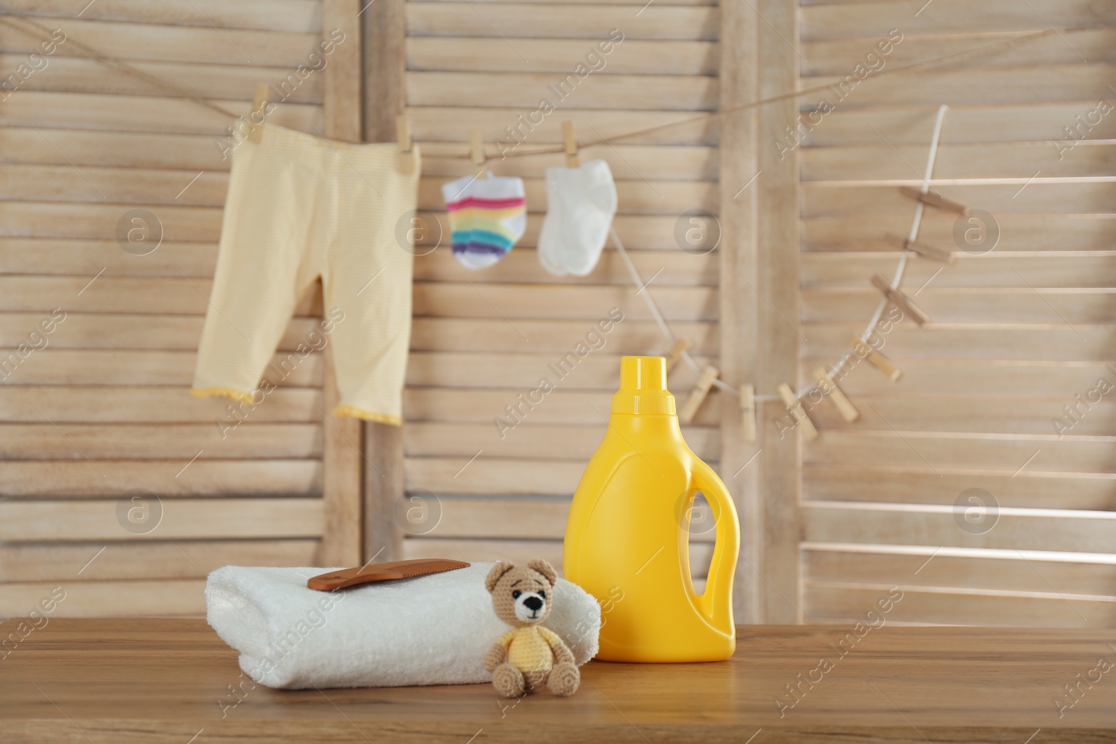 Photo of Fresh baby towel, toy and bottle of detergent on wooden table