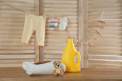 Photo of Fresh baby towel, toy and bottle of detergent on wooden table