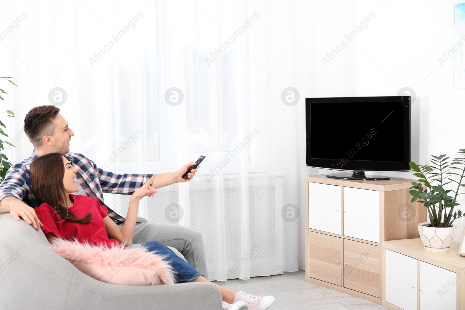 Photo of Happy young couple watching TV on sofa at home