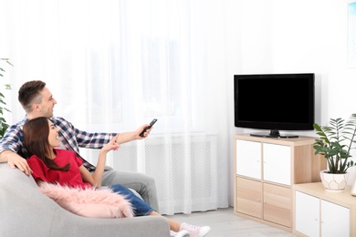 Happy young couple watching TV on sofa at home