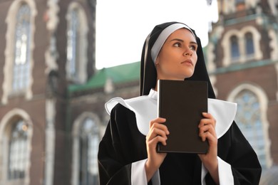 Young nun with Bible near cathedral outdoors on sunny day, space for text