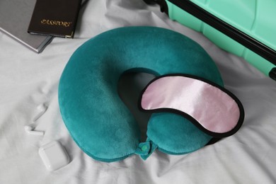 Photo of Turquoise travel pillow with sleep mask, suitcase, passport and earphones on bed