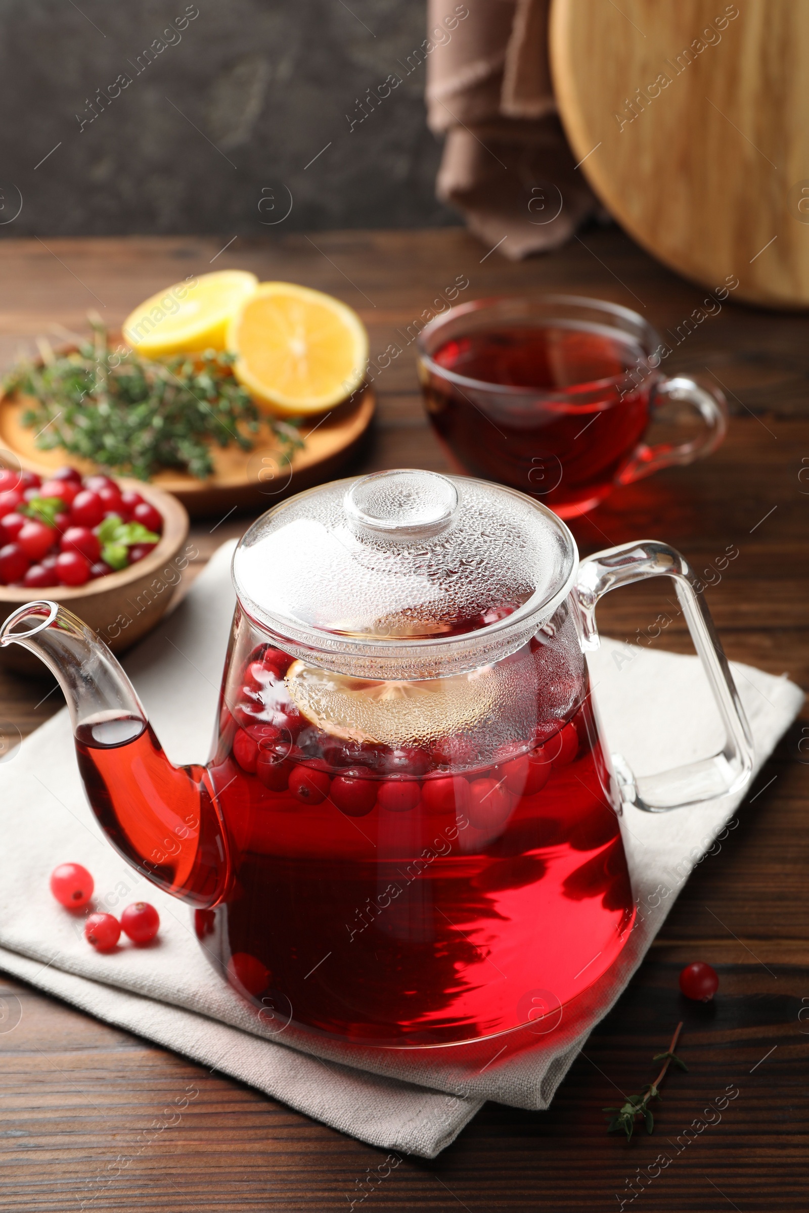 Photo of Tasty hot cranberry tea in teapot and fresh berries on wooden table