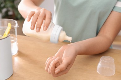 Photo of Woman checking temperature of infant formula at table indoors, closeup. Baby milk