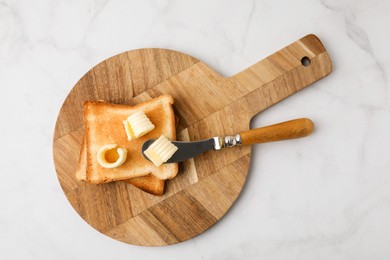 Photo of Tasty butter curls, knife and toasts on white marble table, top view