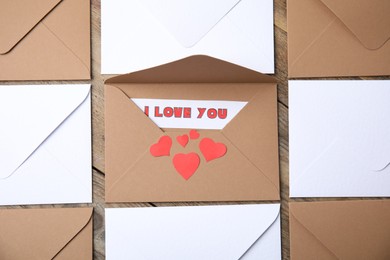 Sheet of paper with phrase I Love You, envelopes and red hearts on wooden table, flat lay