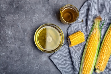 Photo of Flat lay composition with glassware of corn oil and fresh cobs on gray background