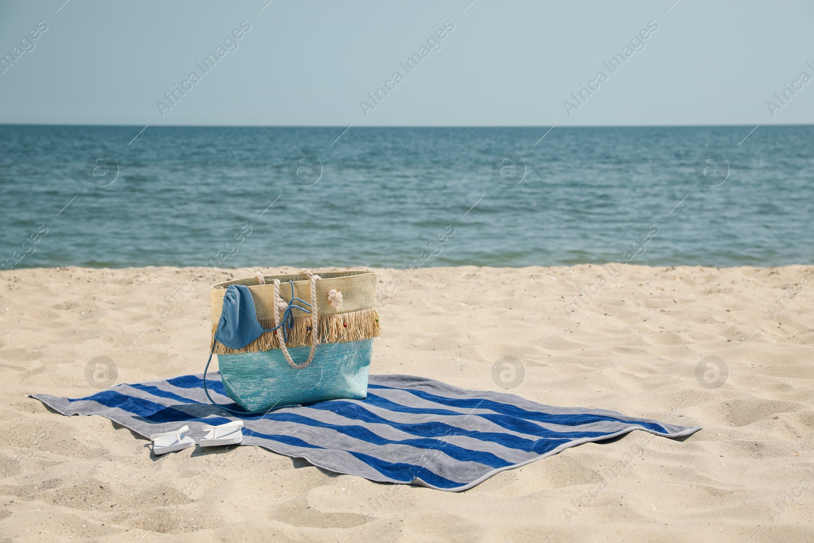 Photo of Beach towel with bag, flip flops and swimsuit on sand