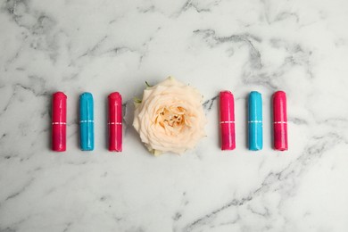 Photo of Colorful tampons and rose on white marble background, flat lay