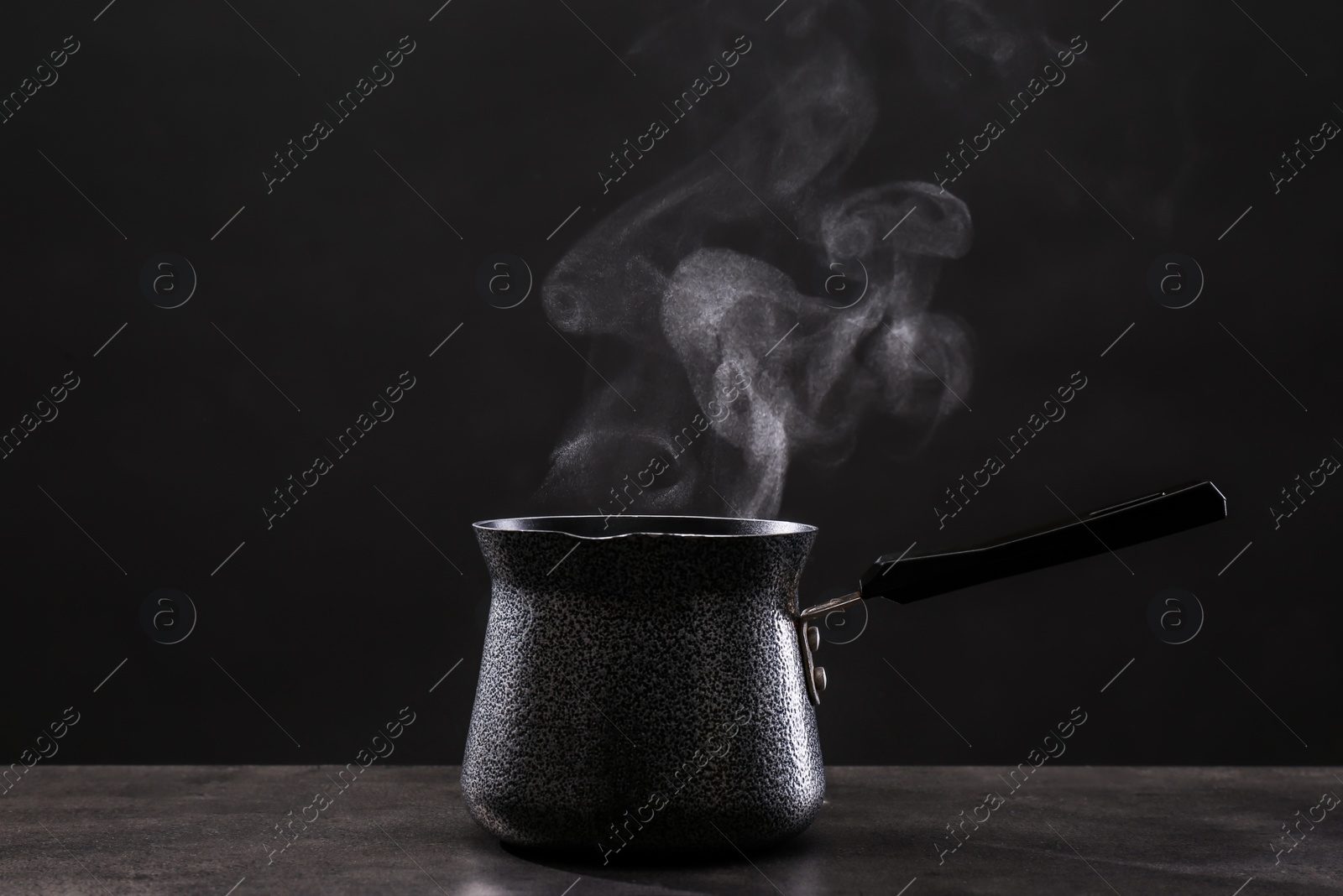 Photo of Steaming cezve on grey table against dark background