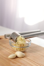 Photo of Garlic press, cloves and mince on wooden table indoors, closeup. Kitchen utensil