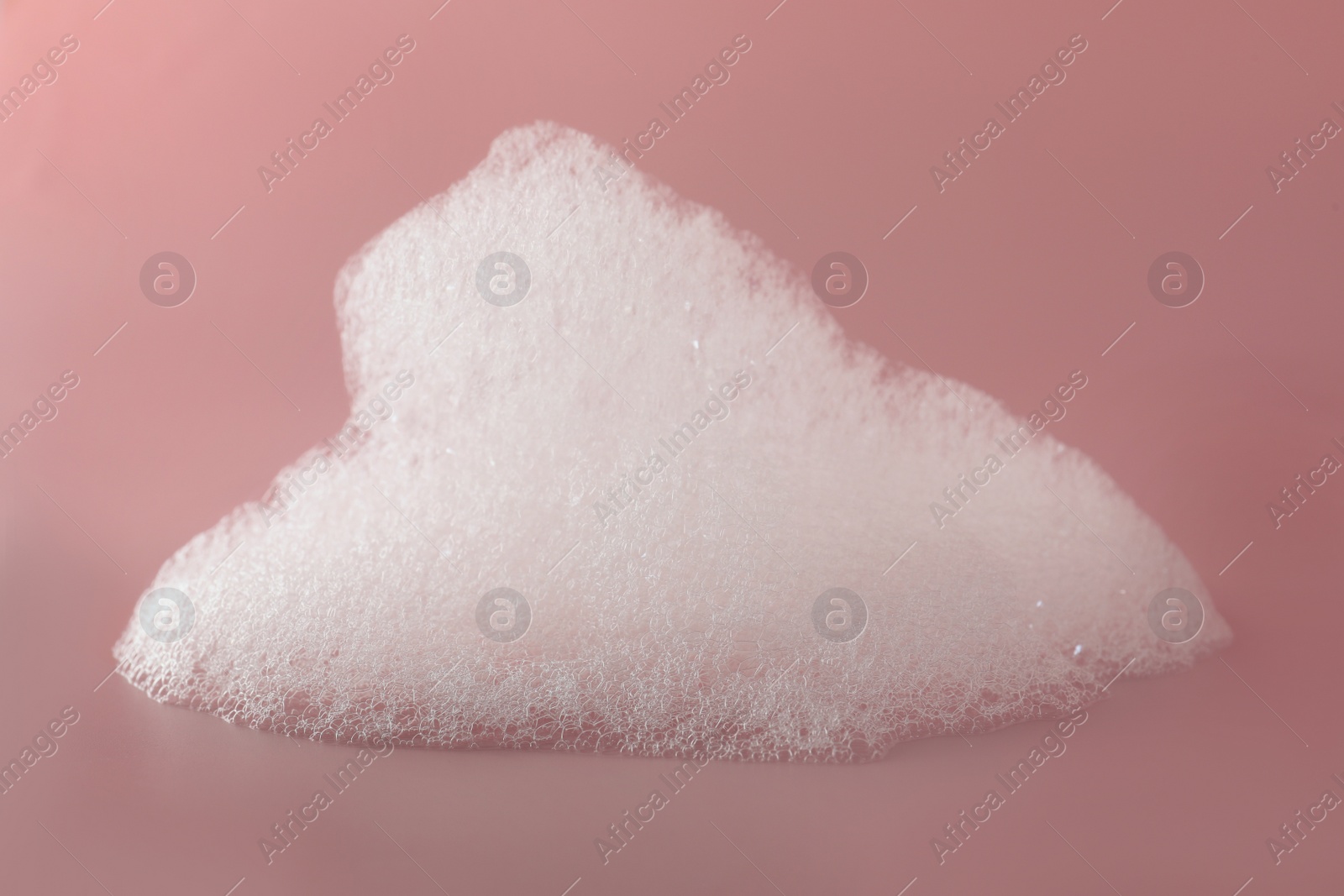 Photo of Fluffy bath foam on pink background, closeup