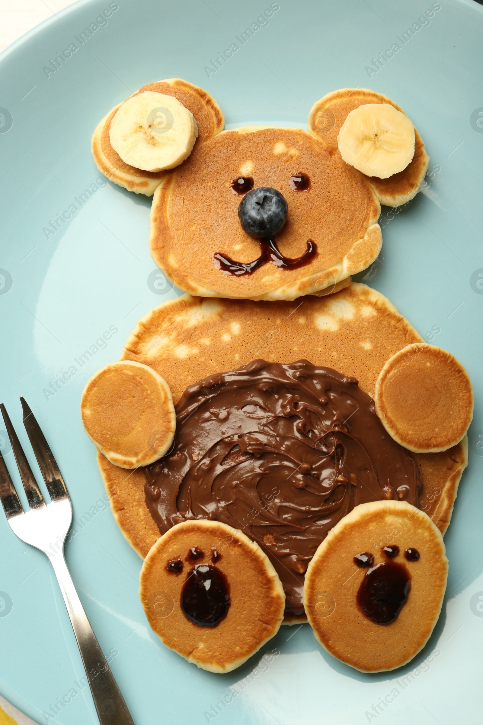 Photo of Creative serving for kids. Plate with cute bear made of pancakes, blueberries, bananas and chocolate paste, top view