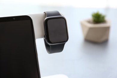 Photo of Stylish smart watch and phone charging with wireless pad against blurred background, closeup. Space for text